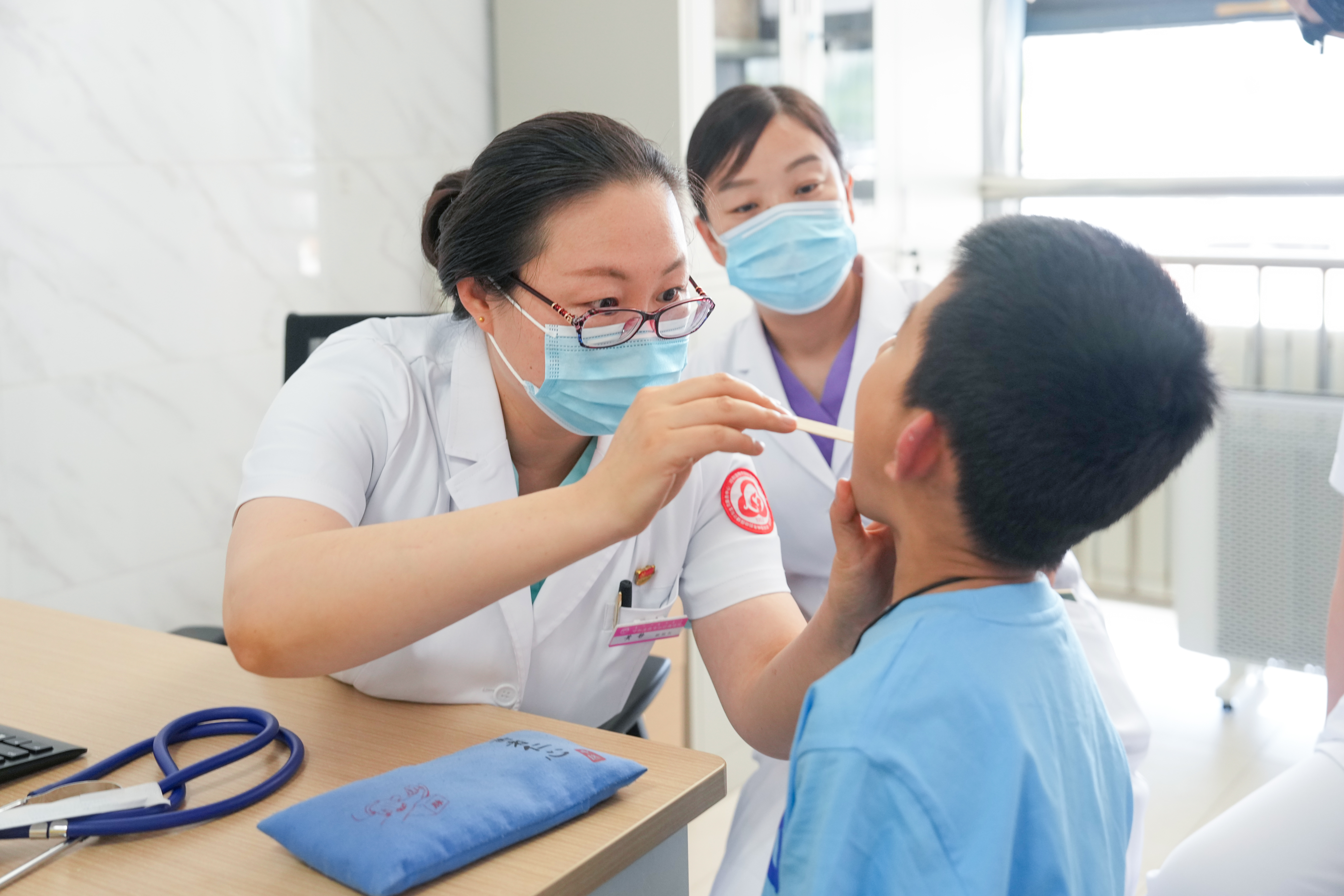 在呼和浩特市婦幼保健院中醫(yī)兒科門診，掛職副院長(zhǎng)黃靜（左一）在細(xì)查看患兒咽喉情況。